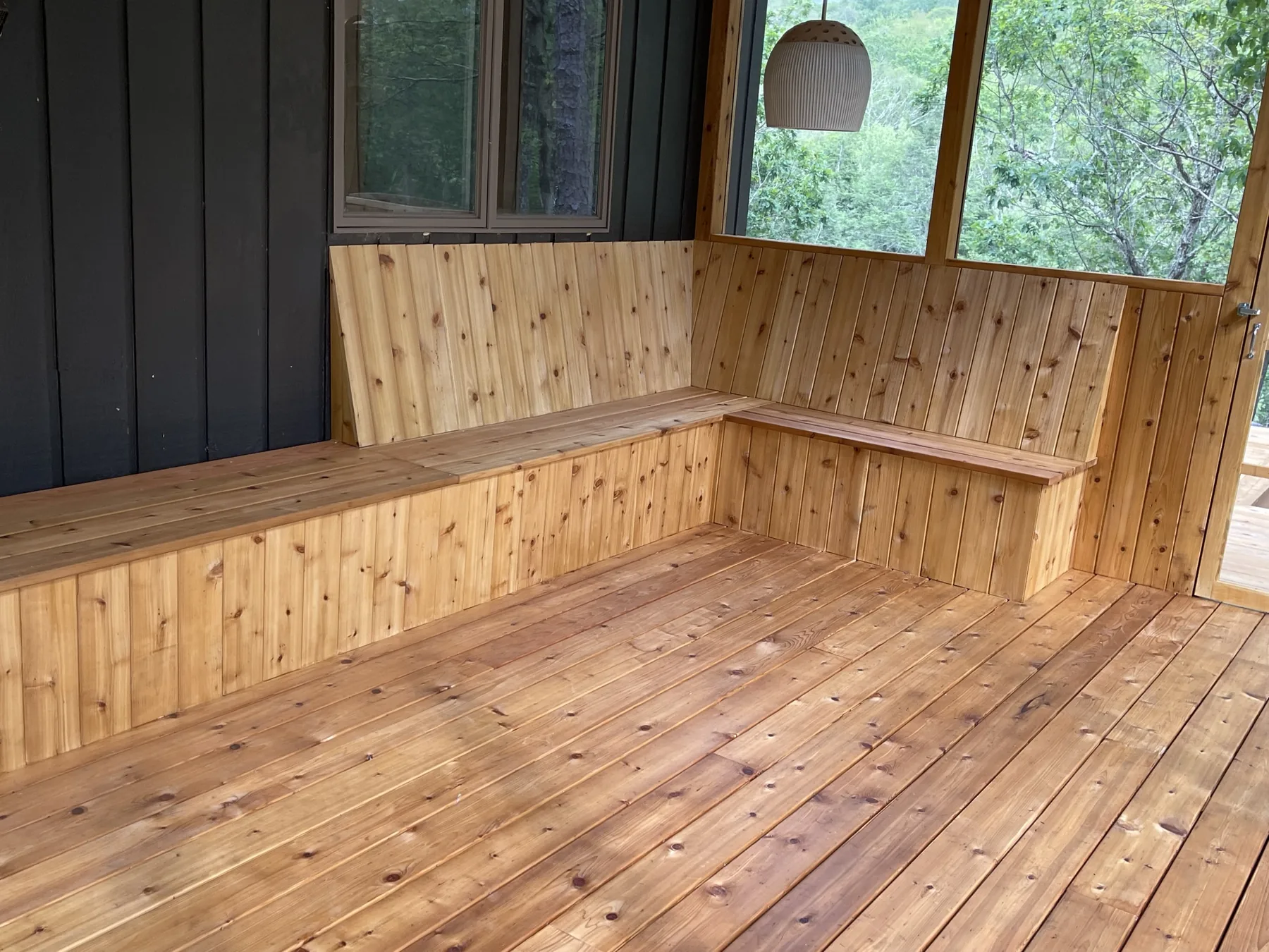 Inside the screened porch: L-shaped built-in cedar bench with a tongue-and-groove back and cedar floor