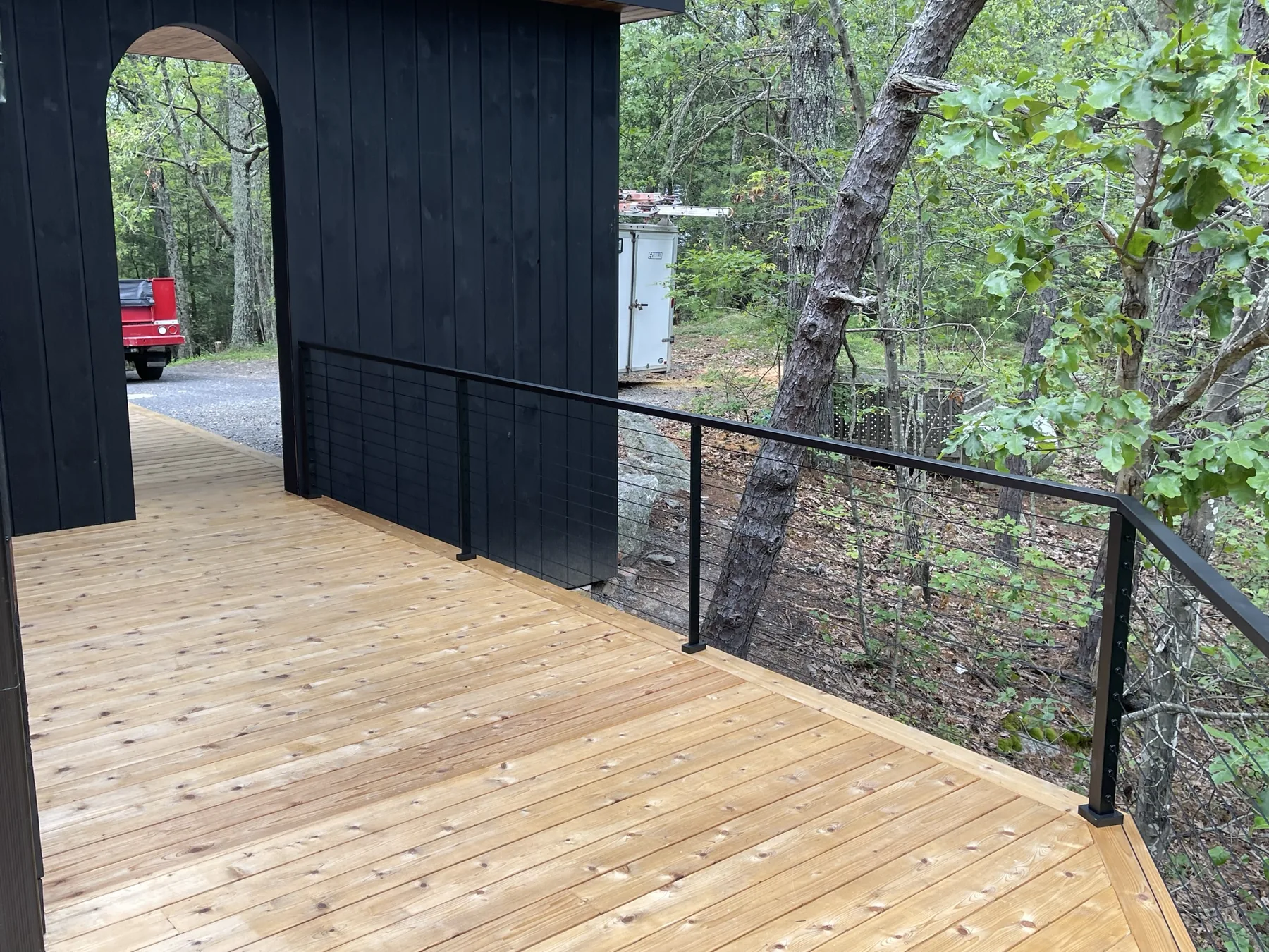 Cedar deck walkway running along the black siding of the house to a black cable railing above the drop