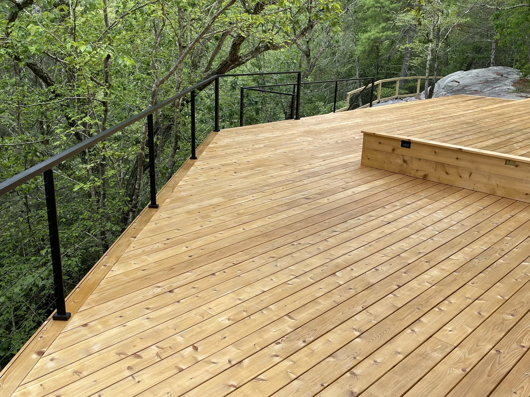 Newly built cedar deck with a black cable railing cantilevered out over a wooded ravine