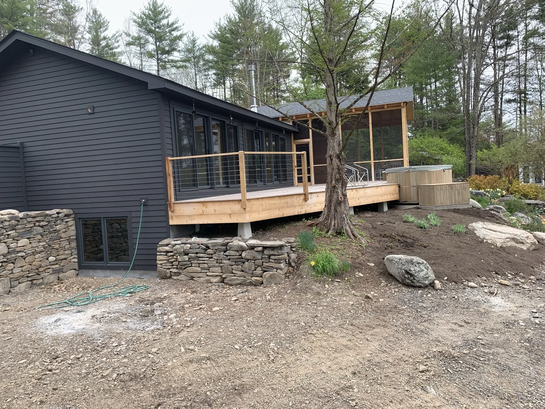 Full view of the renovated house with its new deck, cable railing, screened porch, and dry-stacked stone retaining walls