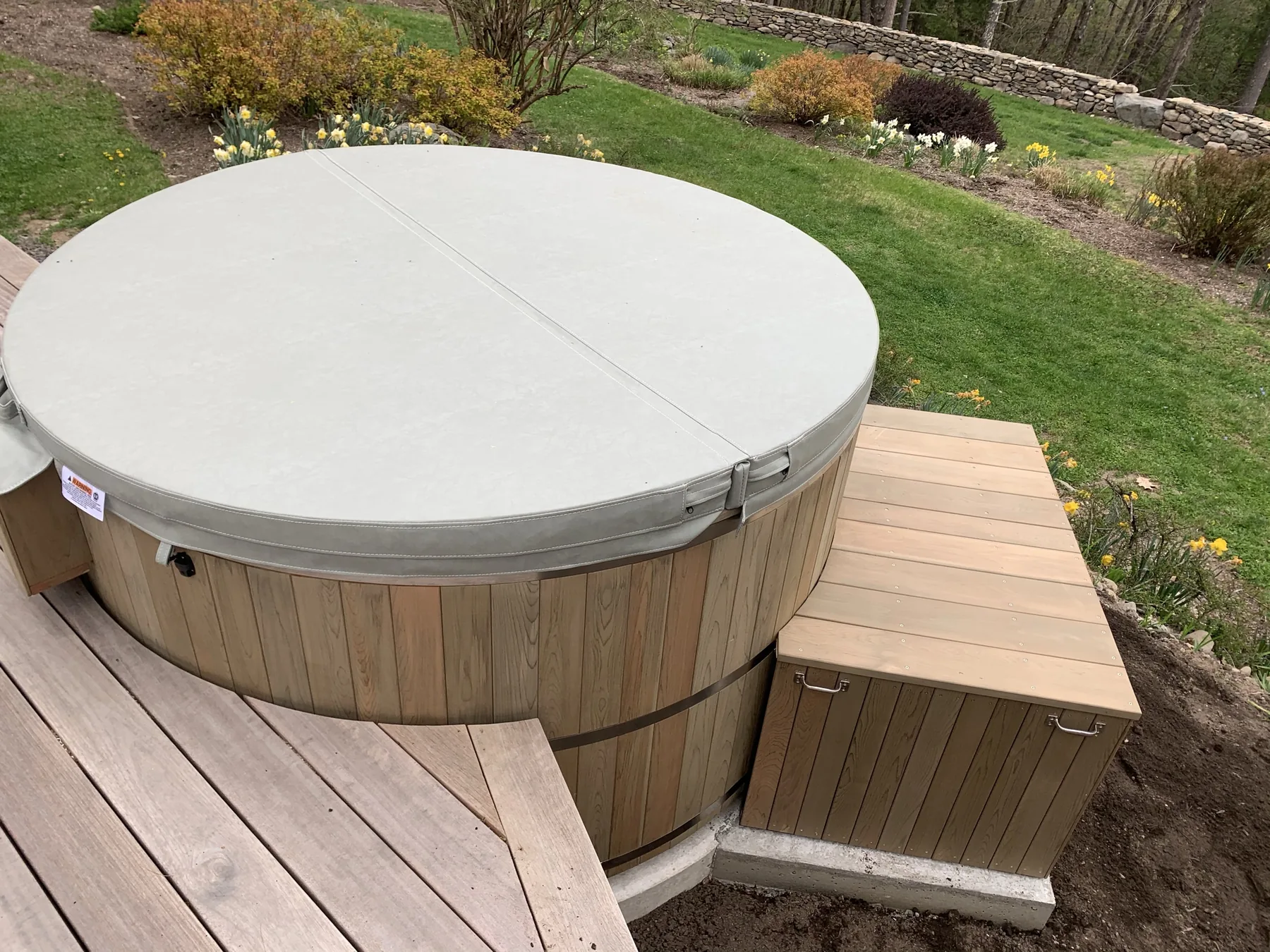 Cedar hot tub with matching deck steps and a hinged equipment enclosure beside a planted bed