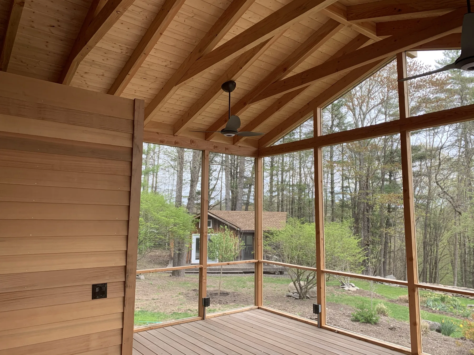 Inside a finished screened porch with an exposed cedar rafter ceiling, ceiling fans, and full-height screen panels looking into the woods
