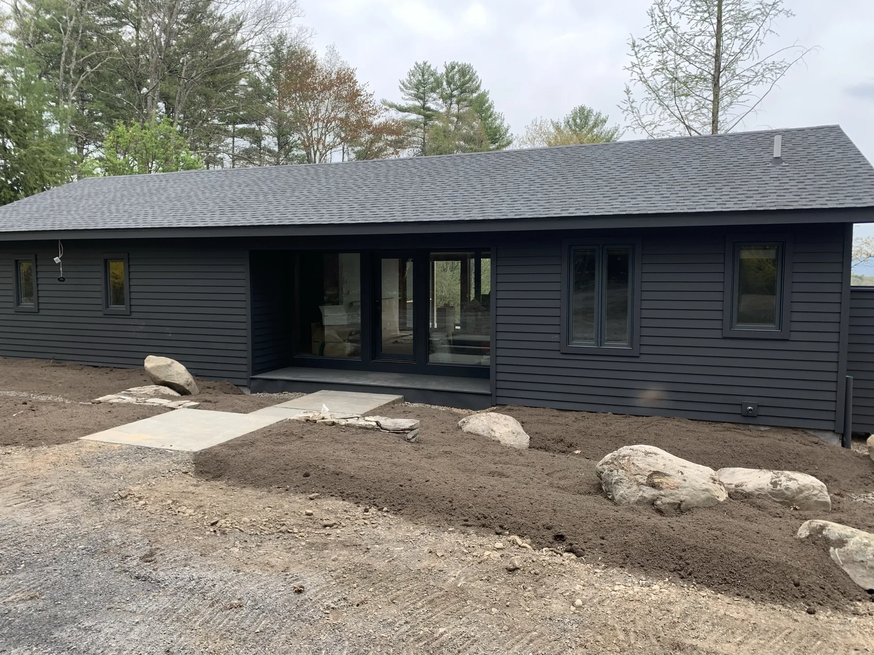 Renovated ranch with dark lap siding, new black-framed windows and sliding doors, and a bluestone entry walk